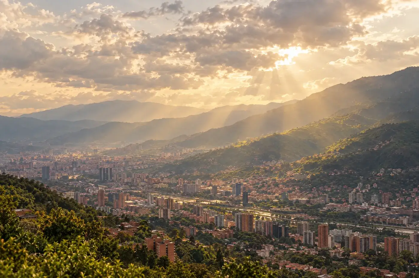 Vista de las montañas del Valle de Aburrá bajo un cielo parcialmente nublado con rayos de sol atravesando las nubes